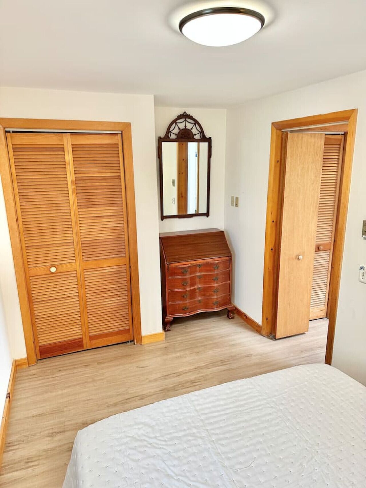Una camera da letto con armadi in legno, una cassettiera, uno specchio e un letto.