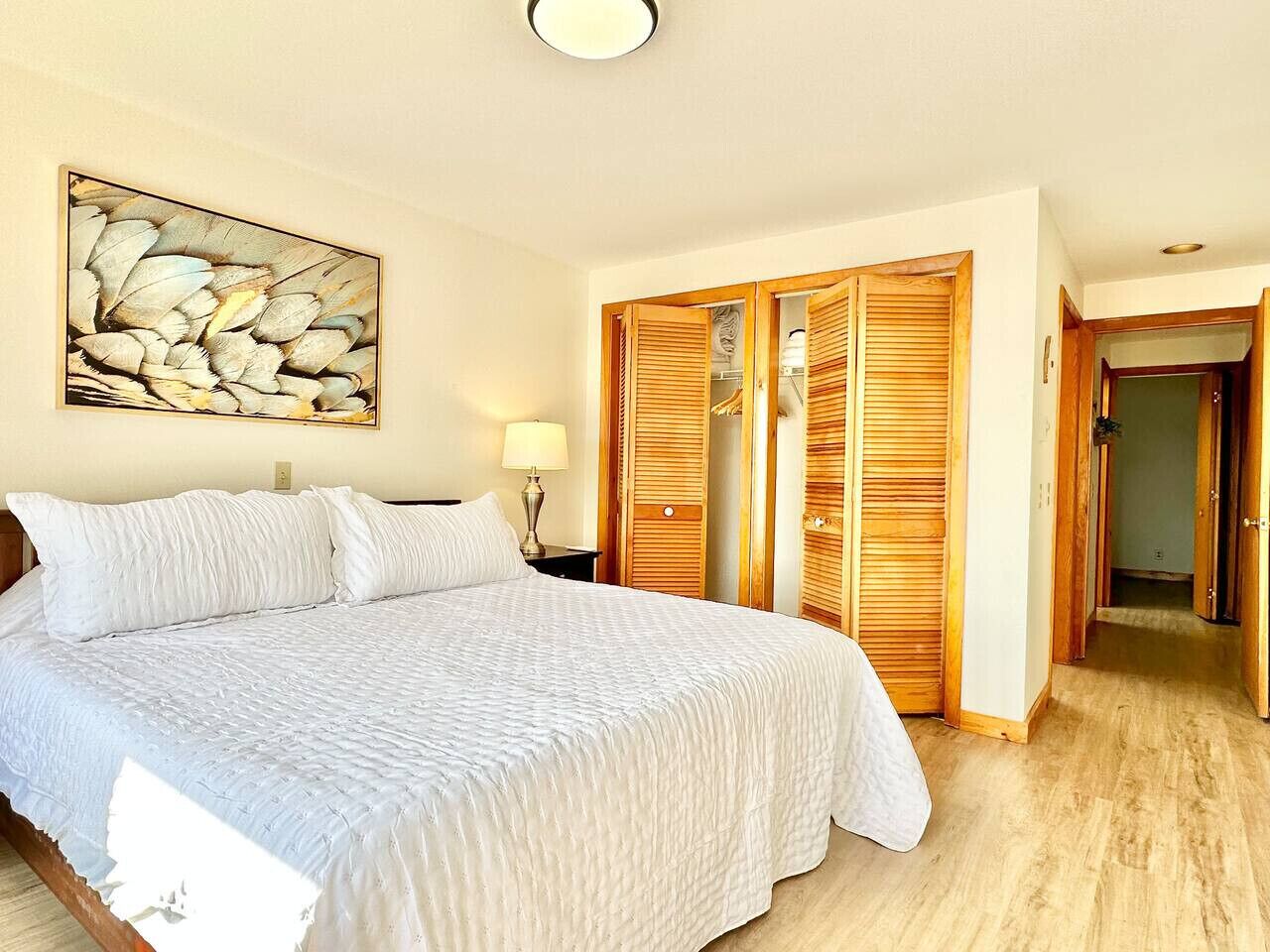 A bedroom with a large bed, wooden wardrobe, and a painting on the wall.