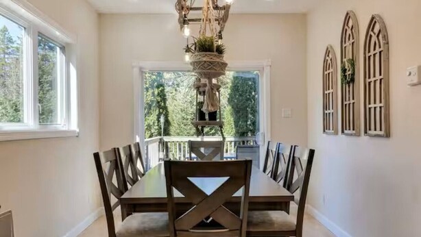 A dining room with a large table and chairs, a chandelier, and three arched windows. - Entire Pine Ridge - 2 Attached Four Bedroom Condos (Bar Harbor)