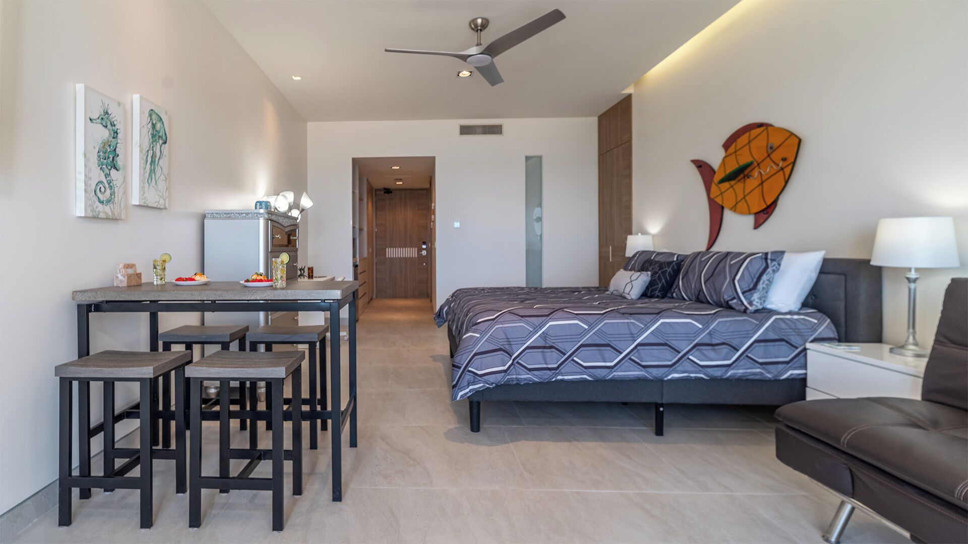 A modern hotel room with a bed, a desk with chairs, a dining area, and artwork on the walls.