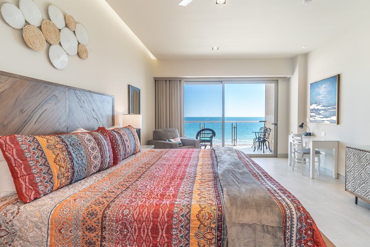 Une chambre spacieuse avec un grand lit, un bureau et une vue sur la mer.