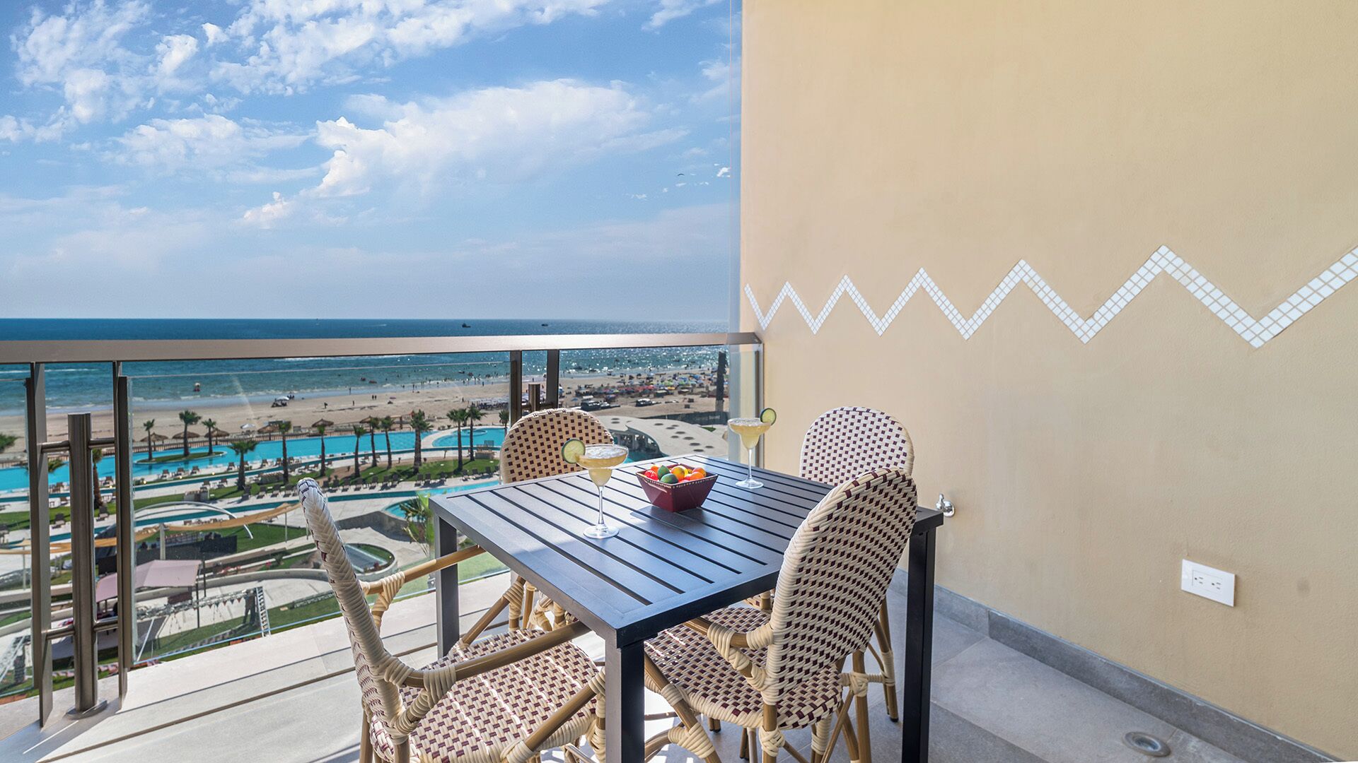 Ein Balkon mit Korbstühlen, einem Tisch und Blick auf Strand und Pool.