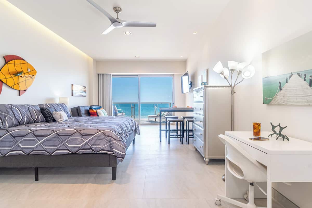 Habitación de hotel moderna con una cama grande, un escritorio y un balcón con vista al mar.