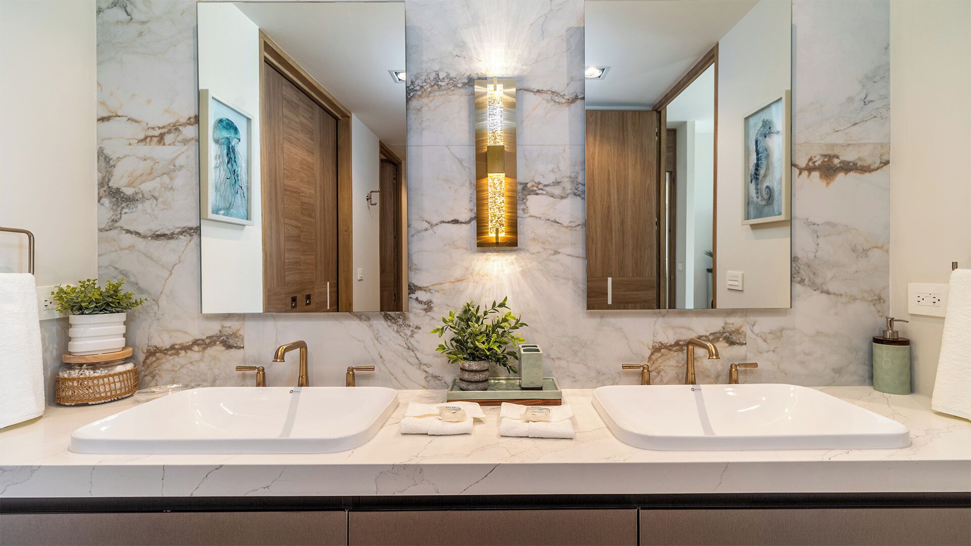 Un baño moderno con dos lavamanos, una lámpara central y obras de arte en las paredes.