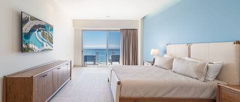 A bedroom with a bed, a nightstand, a wooden dresser, a ceiling fan, and a large window with a view of the ocean.