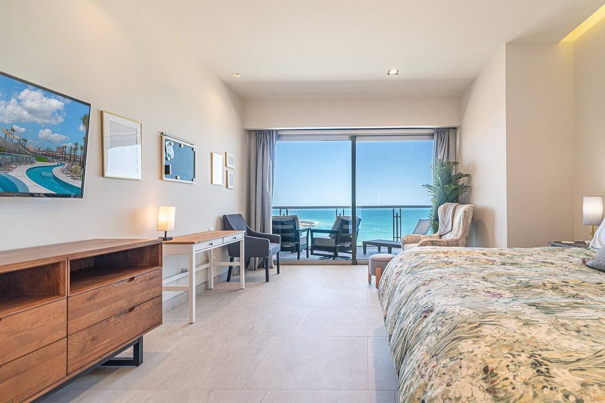 Une chambre d’hôtel avec un lit, un bureau, une chaise, une télévision et une vue sur l’océan.