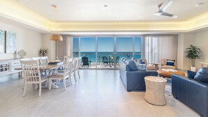 Een ruime woonkamer met een balkon met uitzicht op zee, gemeubileerd met een bank, stoelen en een eettafel.