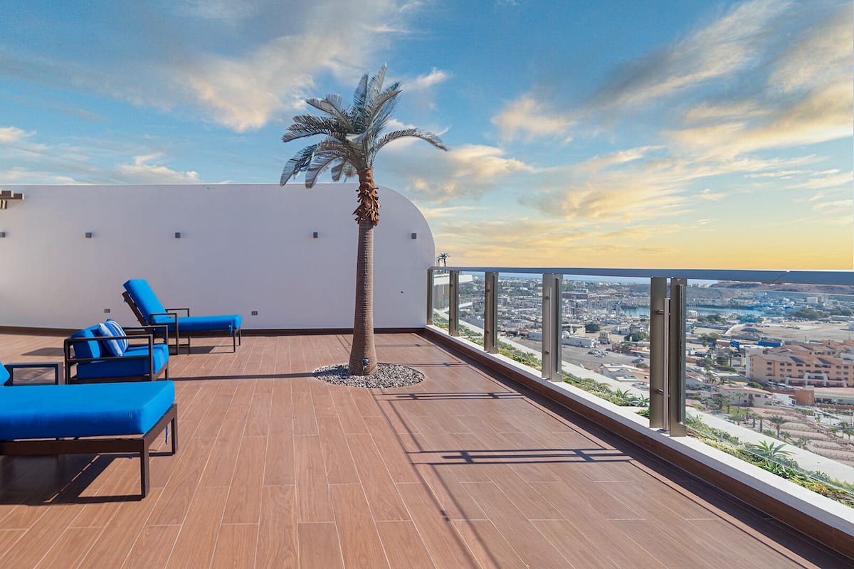 Eine Dachterrasse mit blauen Liegestühlen, einer Palme und Blick auf die Stadt.