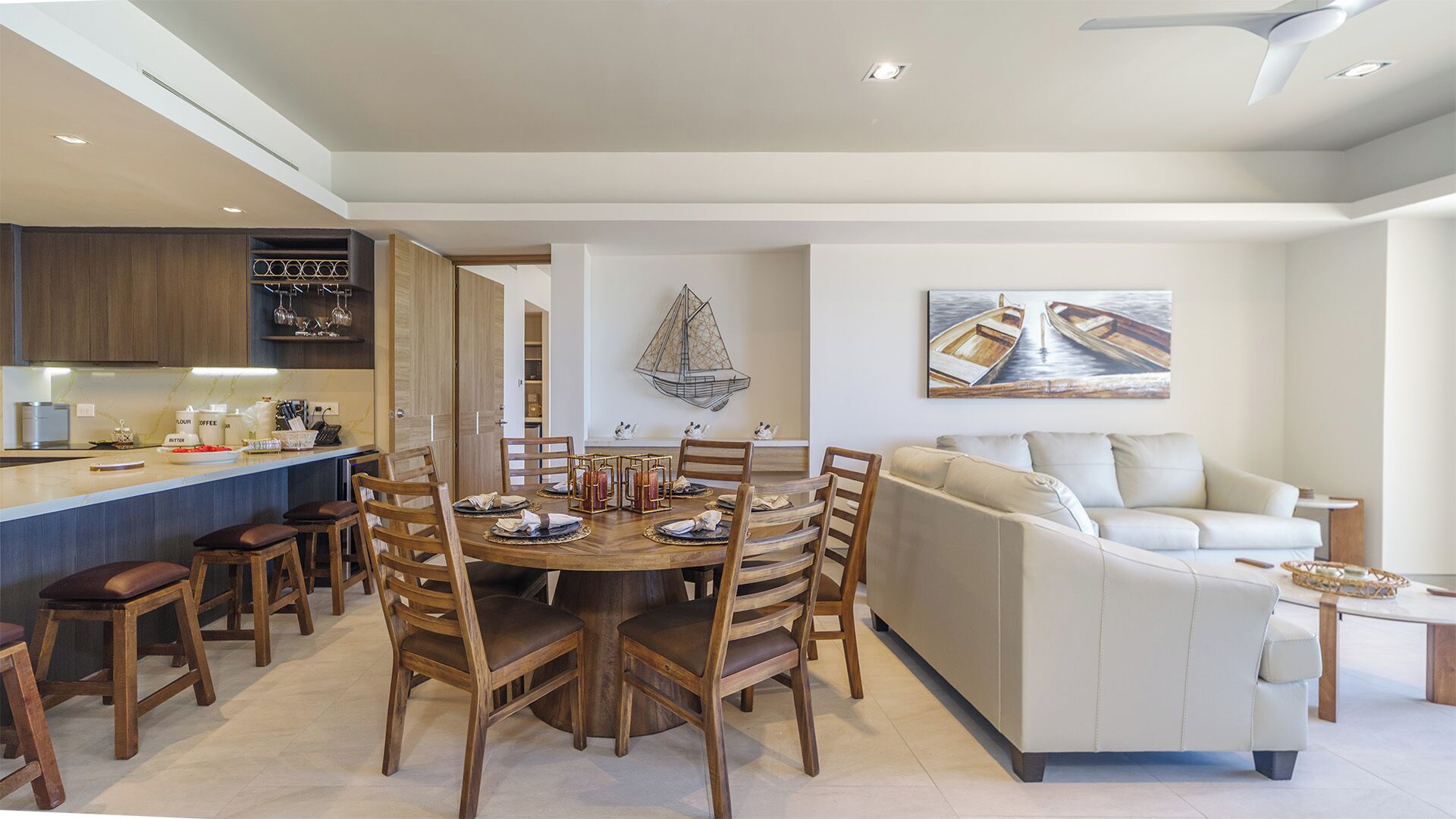 Una sala de estar moderna con comedor, que incluye una mesa redonda de madera, sillas de madera, un sofá color beige y un cuadro con barcos en la pared.