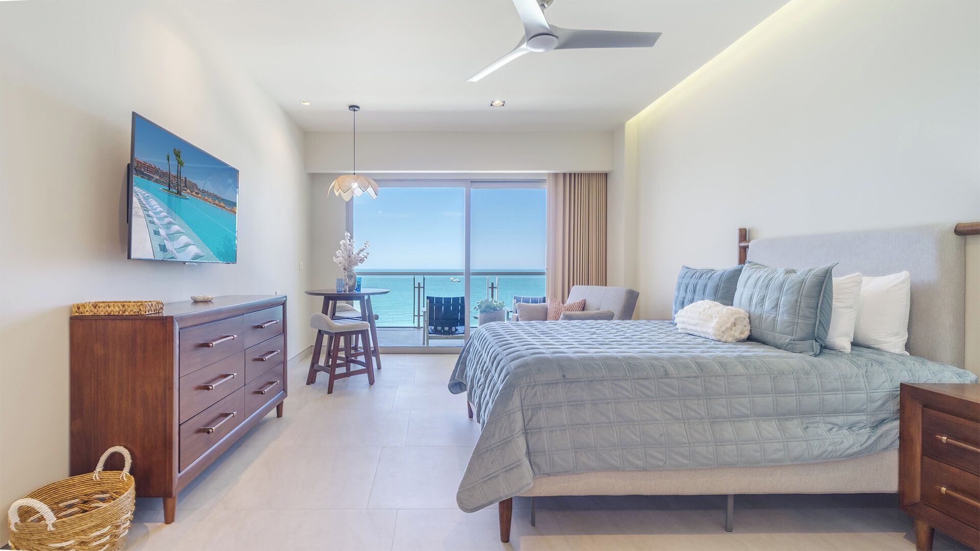 Un dormitorio con una cama grande, un aparador, una silla, una mesa y vistas al océano.
