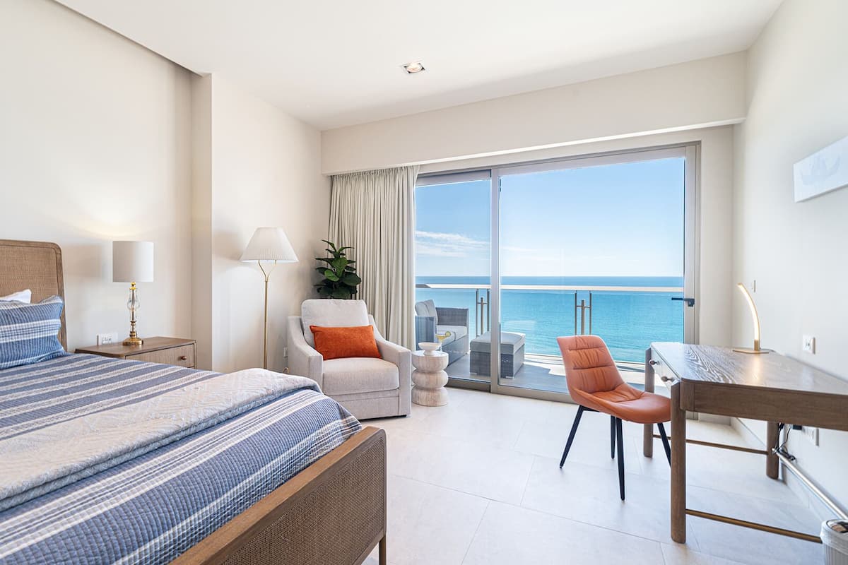 Ein modernes Hotelzimmer mit einem großen Bett, einem Schreibtisch, einem Sessel und einem Balkon mit Meerblick.
