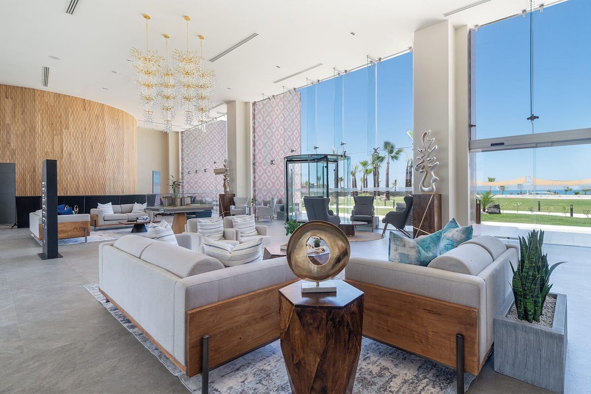 Eine großzügige Lobby mit einer weitläufigen Sitzecke, einer Glaskonstruktion und Blick auf den Strand.