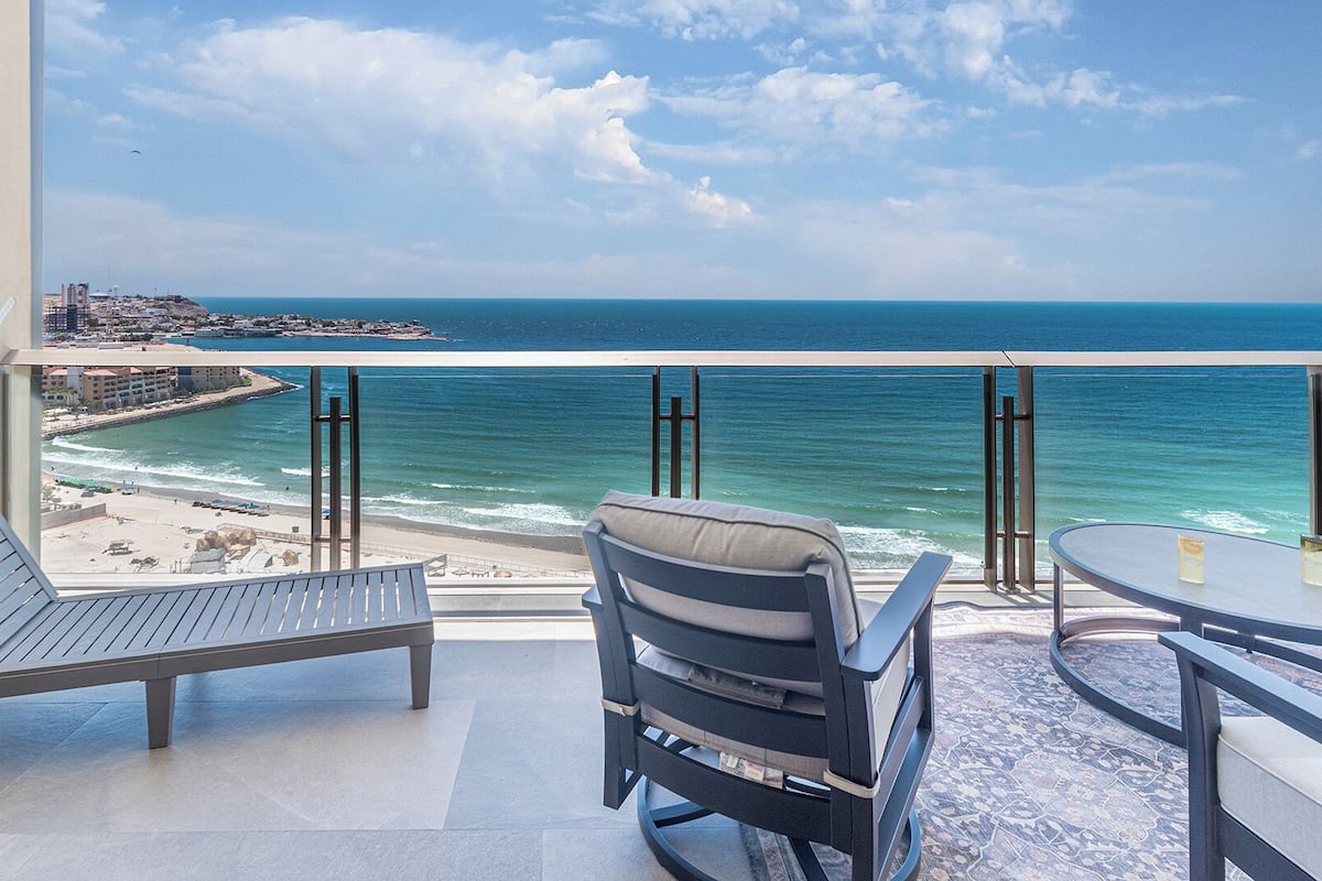 Un balcon avec deux chaises et une table, donnant sur une plage et l’océan.