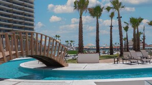 A pool area with a wooden bridge, lounge chairs, and palm trees. - Sonoran Star One (Puerto Peñasco)