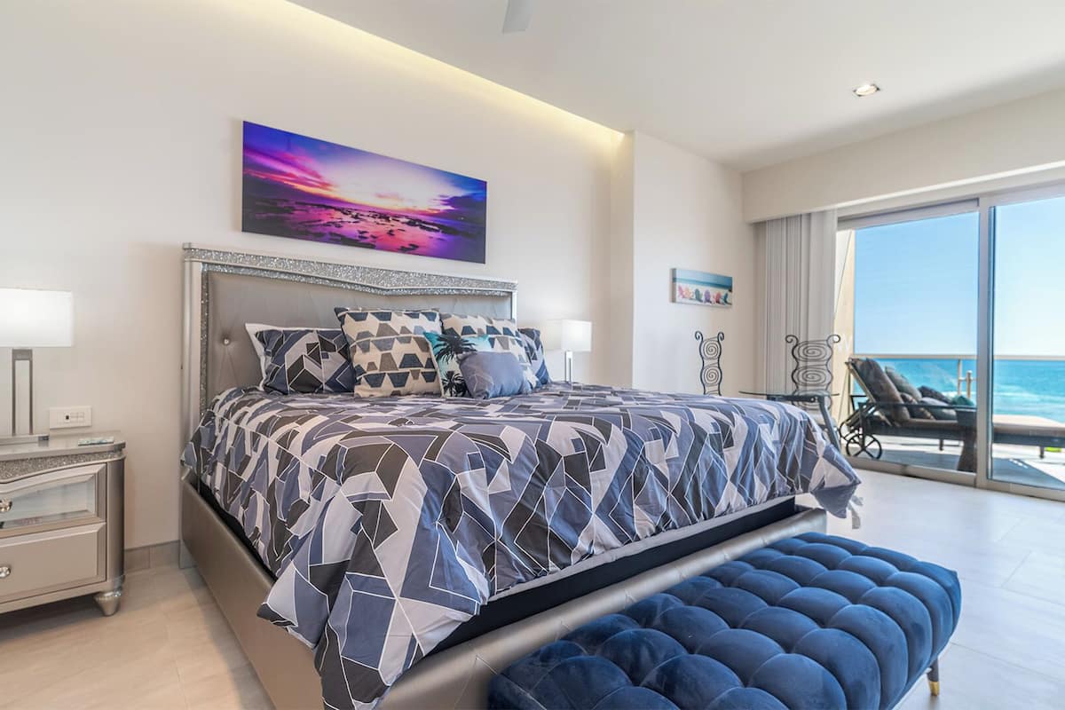Ein modernes Schlafzimmer mit großem Bett, Meerblick und einem Balkon mit Sitzgelegenheit.