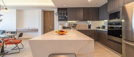 A modern kitchen with a marble island, stainless steel appliances, and a dining area with orange chairs.