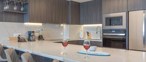 A modern kitchen with a marble countertop, built-in appliances, and a wine glass.