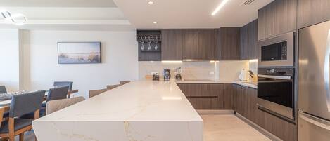 A modern kitchen with a marble island, wooden cabinets, stainless steel appliances, and a dining area with chairs.