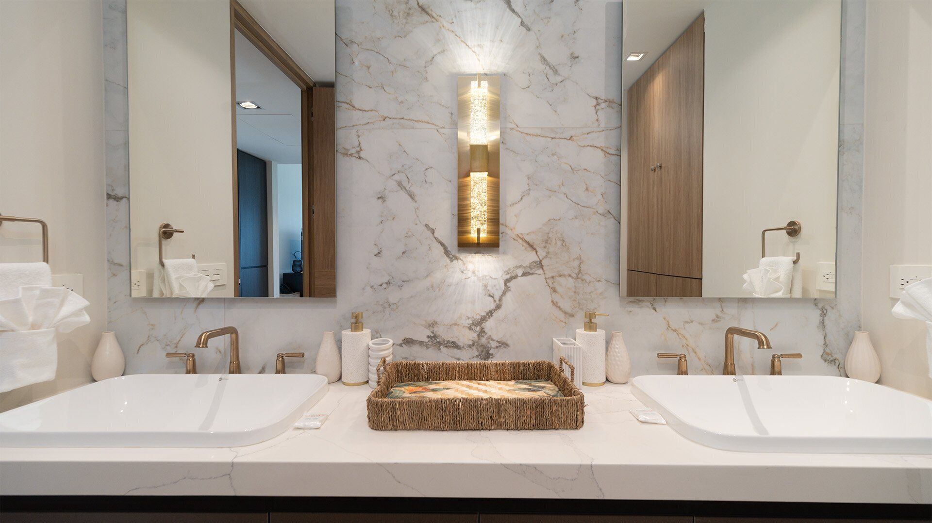 Un baño moderno con dos lavamanos, una salpicadura de mármol y una lámpara central.