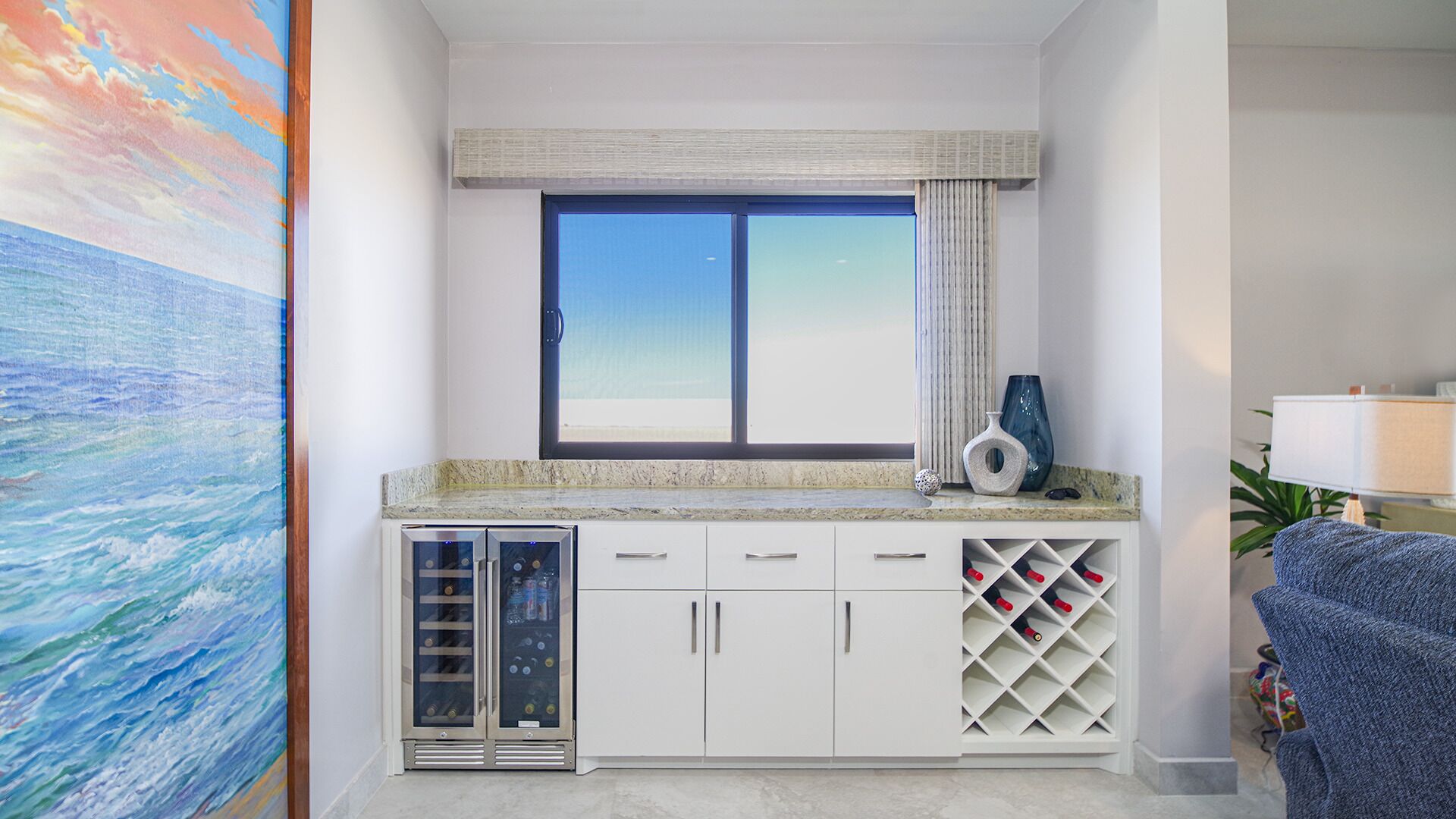 A room with a large window, a wine rack, and a painting.