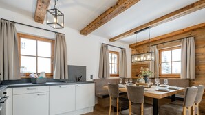 A modern kitchen with white cabinets, a wooden dining table set for four, and large windows with curtains. - Chalet on the Katschberg with sauna (Katschberg)