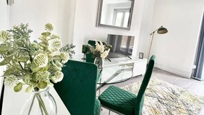 A modern living room with a glass dining table, green upholstered chairs, a large mirror, and a floor lamp. - Penthouse Apartment in Portsmouth: Close to Beach (Portsmouth)