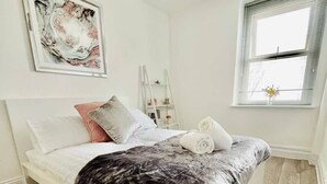 A neatly made bed with a grey blanket and pillows, a white headboard, and a wooden floor. - Penthouse Apartment in Portsmouth: Close to Beach (Portsmouth)