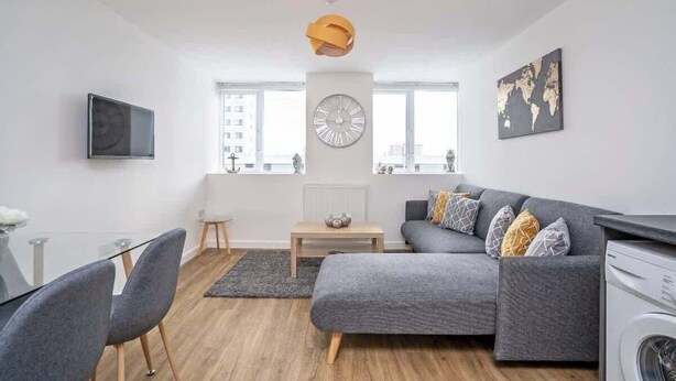 A modern living room with a grey sofa, a round clock, and a world map on the wall.
