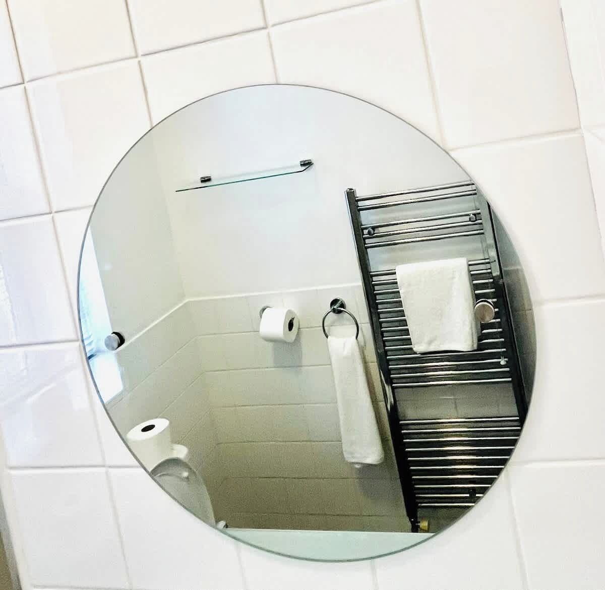 A bathroom with a round mirror, a towel rack, and two rolls of toilet paper.