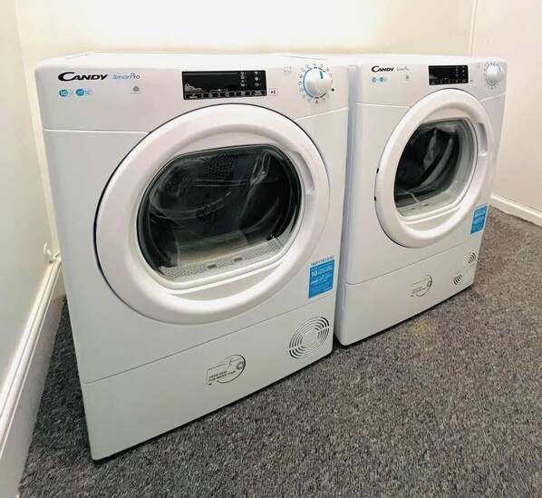 Two Candy SmartPro front-loading washing machines in a corner with a grey carpet floor.