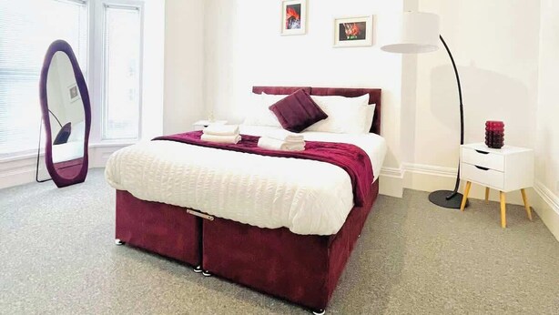 A modern bedroom with a large bed, a bedside table, a floor lamp, and a wall-mounted mirror. - Perfect Portsmouth Getaway Close to Beach (Portsmouth)