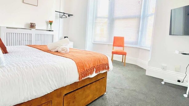 A bedroom with a bed, a window with blinds, a chair, and a TV on the wall. - Southsea Getaway: Close to Beach & Family Fun! (Portsmouth)