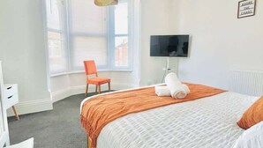 A hotel room with a bed, a desk, a chair, a TV, and a window with blinds. - Southsea Getaway: Close to Beach & Family Fun! (Portsmouth)