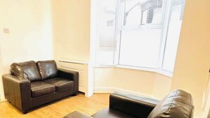 A living room with a black leather sofa, a smaller black sofa, and a window with blinds. - Portsmouth Gem: King Room Close to Beach (Portsmouth)
