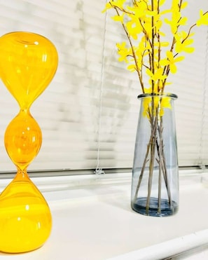 Un sablier en verre transparent et un vase rempli de fleurs jaunes sont posés sur un rebord de fenêtre.