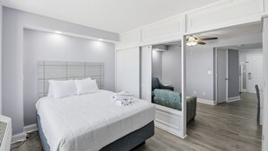 Une chambre d’hôtel moderne avec un grand lit, un coin salon avec un fauteuil et un miroir qui reflète la pièce.