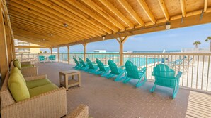 Un espace extérieur abrité, aménagé avec des meubles en osier et des chaises turquoise, donnant sur une plage.