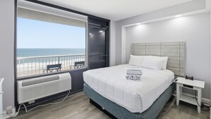 Una camera da letto con un letto, un comodino, una finestra vista spiaggia e una ventola a soffitto.