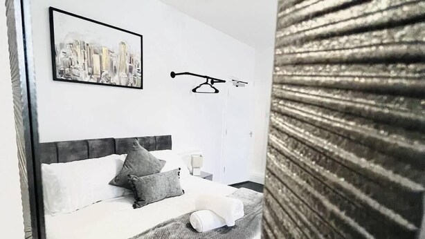 Une chambre moderne avec un lit, des oreillers, un tableau représentant un paysage urbain et un luminaire suspendu.