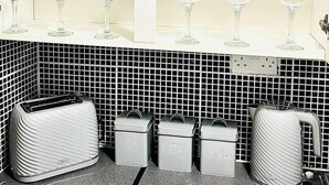 A kitchen with white shelves holding glassware and bowls, a tiled backsplash, and labeled storage containers for tea, coffee, and sugar. - Portsmouth Apartment: Family friendly with Parking (Portsmouth)