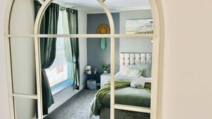 Une chambre à coucher avec un lit, des rideaux, une table de chevet, une plante et une fenêtre.
