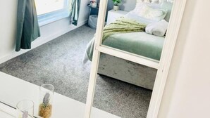 Une chambre à coucher avec un lit, une table de chevet, un miroir et une fenêtre avec des rideaux.