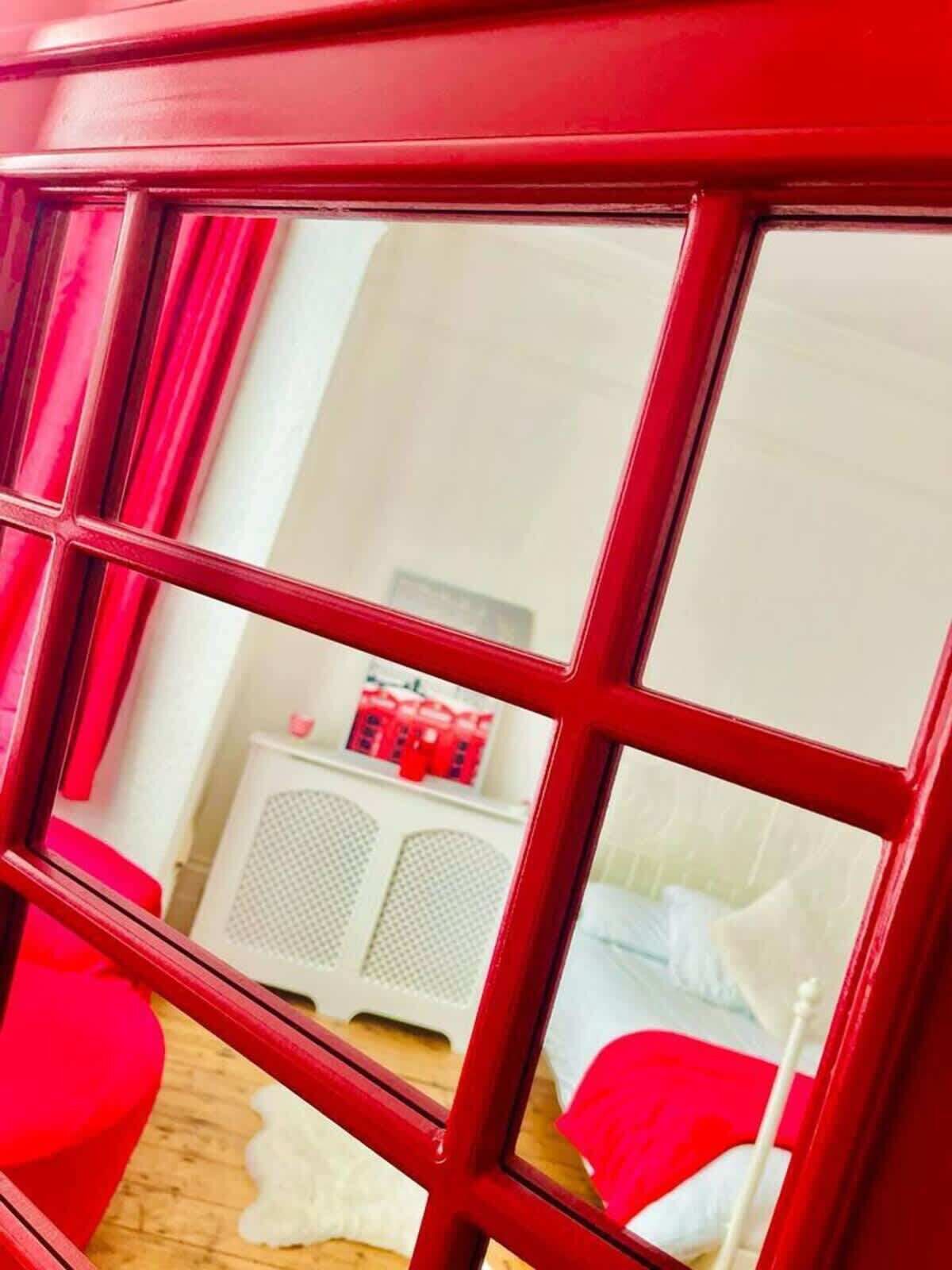 A room with a red-framed window, a white cabinet, and a bed with red bedding.