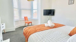 Ein Hotelzimmer mit Bett, Schreibtisch, Stuhl, Fernseher und Fenster mit Jalousien.