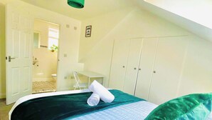 A bedroom with a skylight, a bed with a green pillow, a rolled towel, and a small desk with a chair.