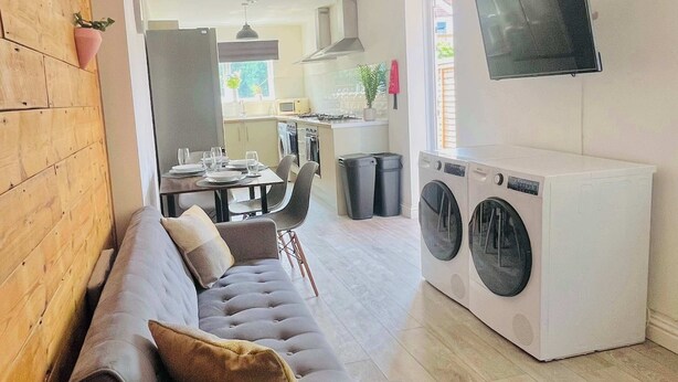 A modern living room with a grey sofa, a washing machine, and a TV mounted on the wall.