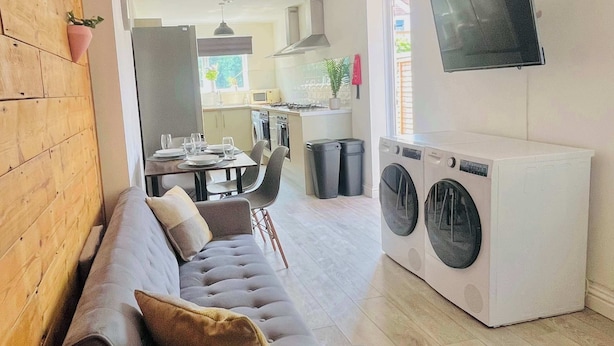 A modern living room with a grey sofa, a washing machine, and a TV mounted on the wall. - Cleveland Road House: Comfort & Convenience (Portsmouth)