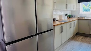 A kitchen with a stainless steel refrigerator, light-colored cabinets, a wooden countertop, and a black hanging light fixture. - Cleveland Road House: Comfort & Convenience (Portsmouth)
