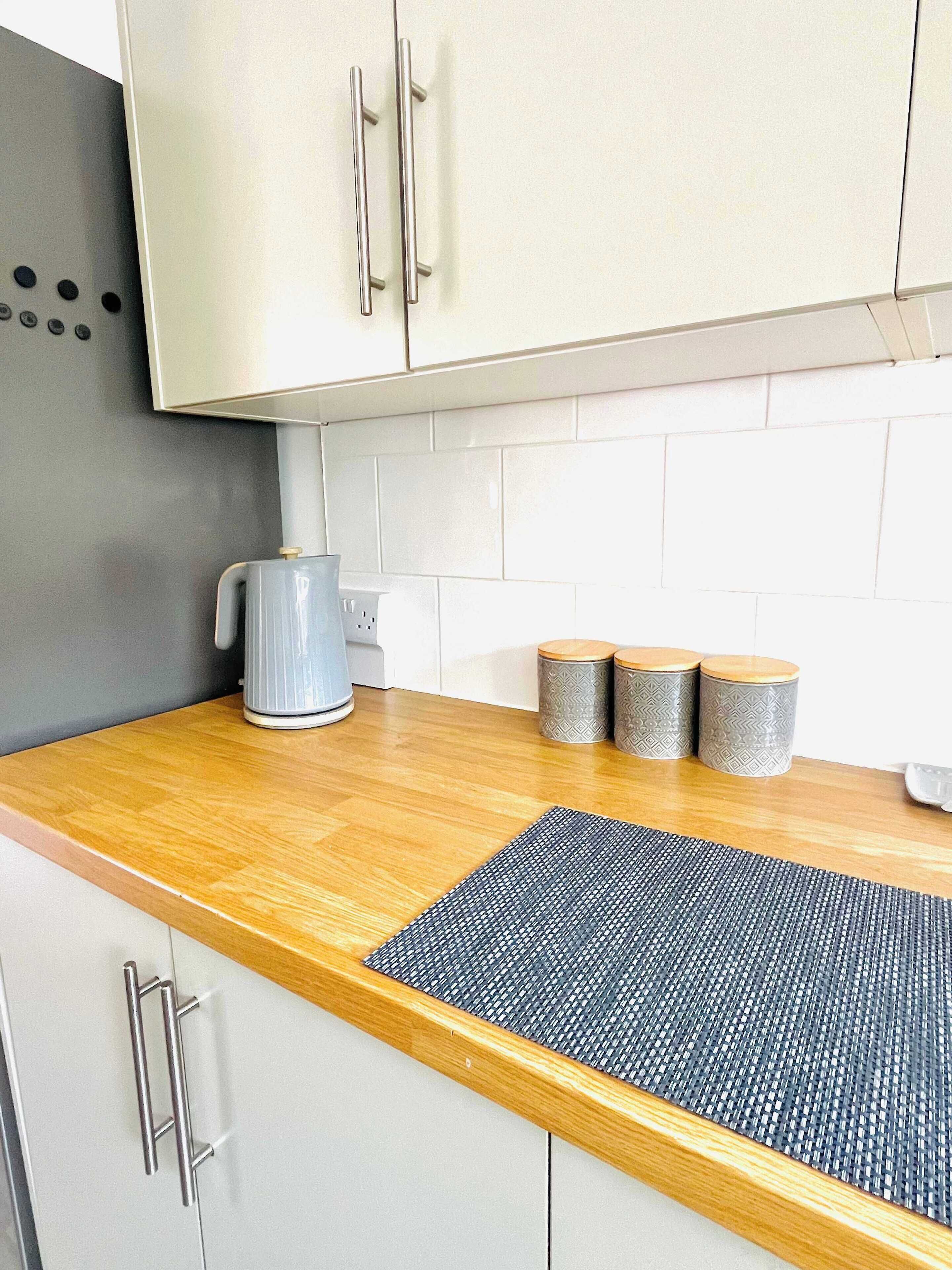 Una cocina con encimera de madera, una cafetera y tres recipientes decorativos.
