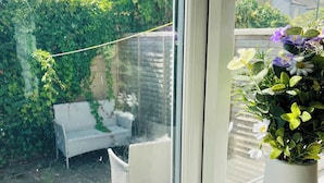 A window with a view of a garden, a white chair, and a potted plant with flowers. - Cleveland Road House: Comfort & Convenience (Portsmouth)